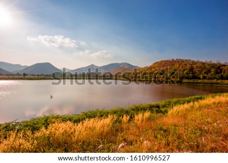 Panoramic nature wallpaper Of a large lake grass field, surrounded by mountains, trees, bright blue skies, blurred winds, cool atmosphere