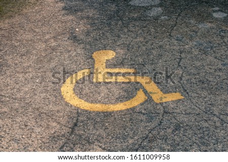 Yellow handicapped symbol of wheelchair painted on gray asphalt on a parking lot, sign of parking space for disabled visitors. Free parking for disabled people's car. Empty disabled parking space.