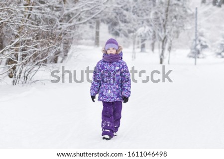 Adorable young girl walking in beautiful winter park during snowfall. Cute child playing in a snow. Winter activities for family with kids.