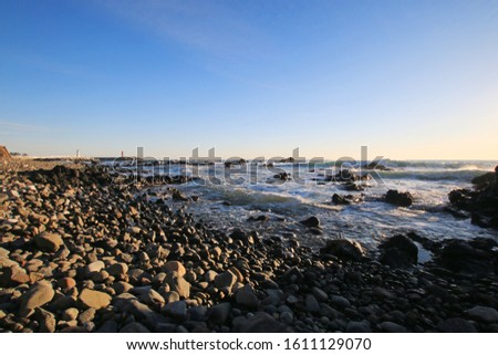 a picture of a beach with gray stones against the blue sea and sky.