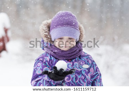 Adorable young girl having fun in beautiful winter park during snowfall. Cute child playing with a snow. Winter activities for family with kids.