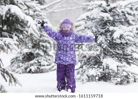 Adorable young girl having fun in beautiful winter park during snowfall. Cute child playing in a snow. Winter activities for family with kids.