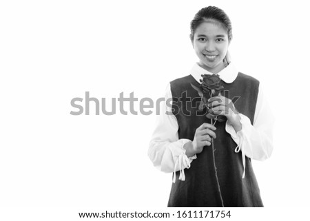 Studio shot of young happy Asian woman smiling while holding red rose