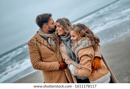 A beautiful married couple and their lovely daughter are hugging on the seashore, dressed in coats in the cold season.