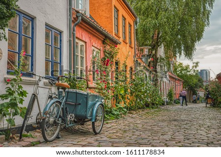 On a summer day a typical Danish Cargo bike, better known as Christiania Bike, is parked at the entrance of a house in a cosy, cobbled street conveying coziness and cultural concept - Aarhus, Denmark Royalty-Free Stock Photo #1611178834