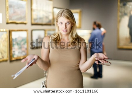 Woman wearing glasses throwing up her hands near the picture in art museum hall