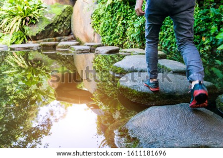 Young man walking crossing a river on stones. Royalty-Free Stock Photo #1611181696