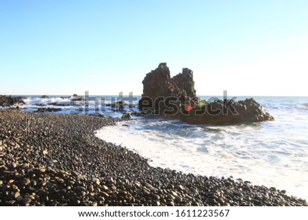 It is a picture of large gray rocks and small rocks against the backdrop of the sea. And the sunlight is reflected on the lens and shining on the rock.