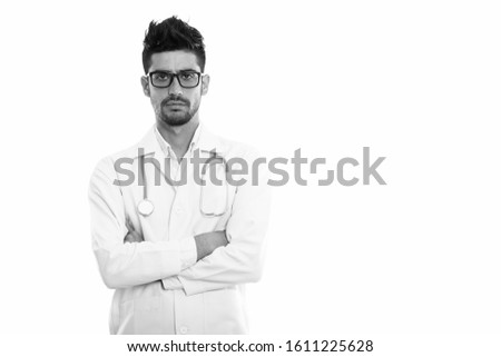 Studio shot of young Persian man doctor wearing eyeglasses with arms crossed