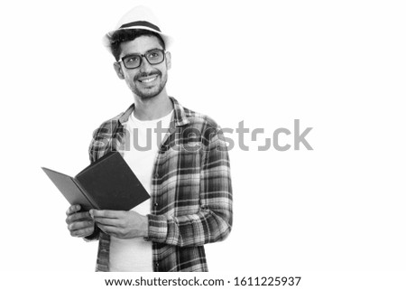 Studio shot of young happy Persian man smiling while holding book and thinking