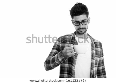 Studio shot of young Persian man holding and looking at coffee cup