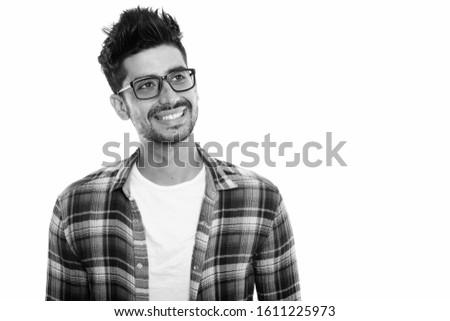 Studio shot of young happy Persian man smiling while wearing eyeglasses and thinking