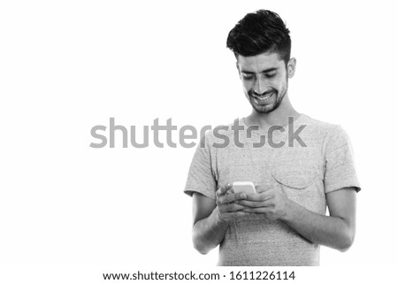 Studio shot of young happy Persian man smiling while using mobile phone