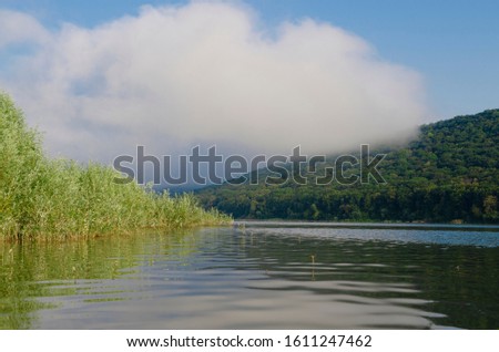 Morning fog over the mirrored mountain river against the background of mountains and blue sky
