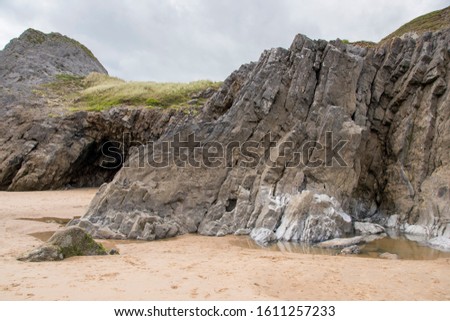 A craggy little cave opening in the cliff face at Three Cliffs Bay, The Gower Peninsula, Wales Royalty-Free Stock Photo #1611257233
