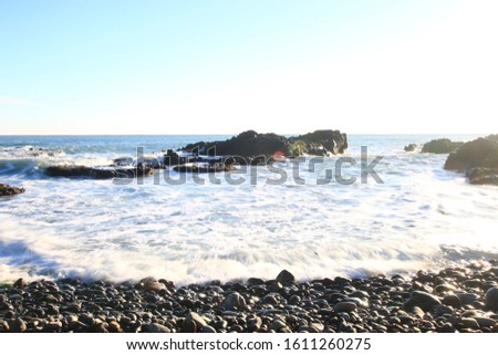 It is a picture of large gray rocks and sea water against a background of blue sky and sea. And the sunlight reflects on the lens and shines on the rock. a photo taken with a bright exposure