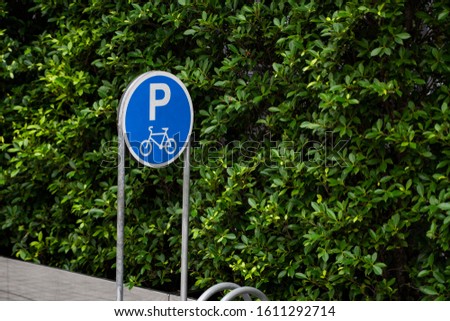 Empty stainless steel bicycle parking rack with a sign of bicycle parking with a green plants on a wall.