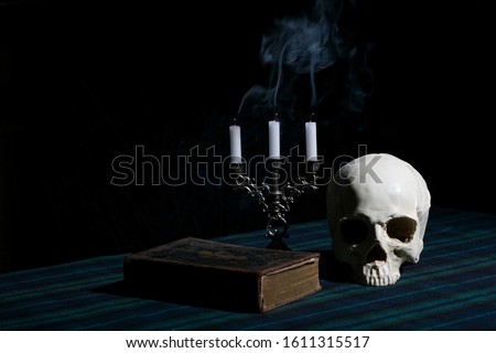 A skull, candles in a candelabrum and an old book on a table