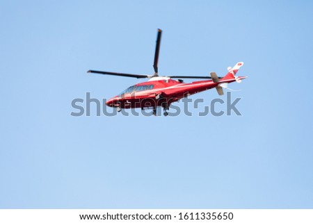 Side view of small red private helicopter against a blue sky with spinning propellers