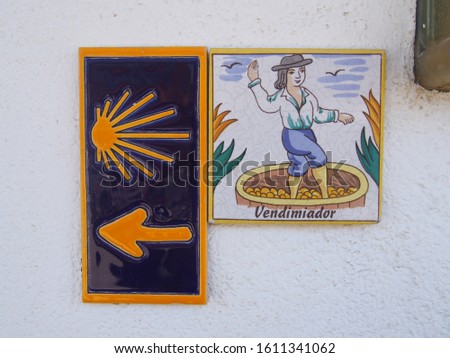 Yellow scallop shell mark with arrow sign and grape picking picture, Camino de Santiago, Way of St. James, Journey from Ponferrada to Villafranca del Bierzo, French way, Spain