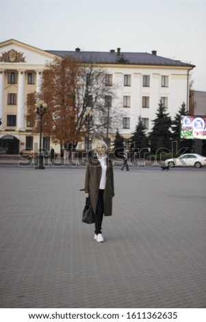 
A blonde girl in a green coat is walking through the autumn city.