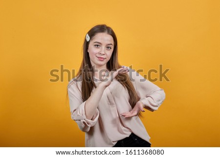 Calm young woman showing space between palms, looking at camera wearing fashion pastel shirt isolated on orange background in studio. People sincere emotions, lifestyle concept.