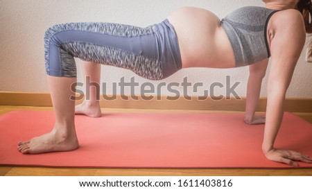 Pregnant woman's belly close up. A pregnant young redhead woman is exercising yoga at home preparing for the childbirth and expecting her first baby. Concept of a new life, expectations and hope.