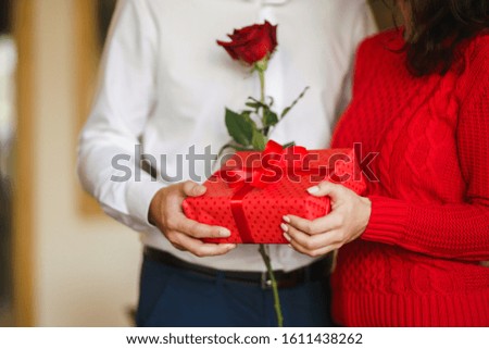 Red gift box in the hands of a couple in love. Valentine's Day, holiday and surprise concept. Lovers give each other presents. Relationship and love concept.