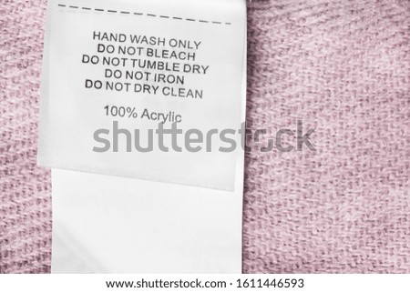 Care and composition clothes label on knitted pink background closeup