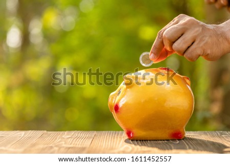 Close up hand put the coin to piggy bank with green nature blur background. Money savings concept
