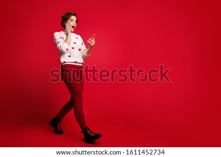 Full length body size view of her she nice attractive amazed impressed cheerful cheery girl walking using cell reading feedback comment isolated over bright vivid shine vibrant red color background
