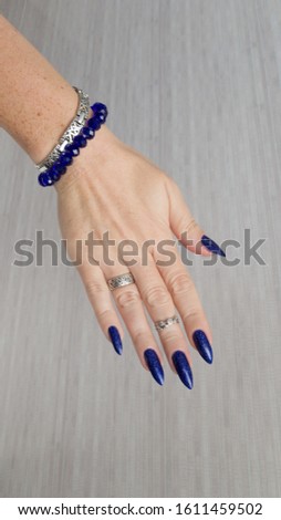 Female hand with long nails and blue manicure with bottles of nail polish