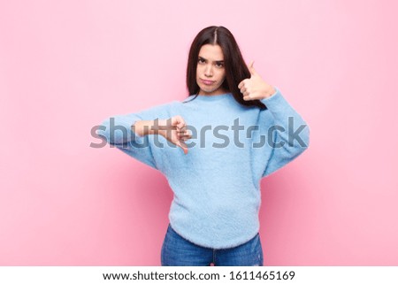 young pretty woman feeling confused, clueless and unsure, weighting the good and bad in different options or choices against pink wall
