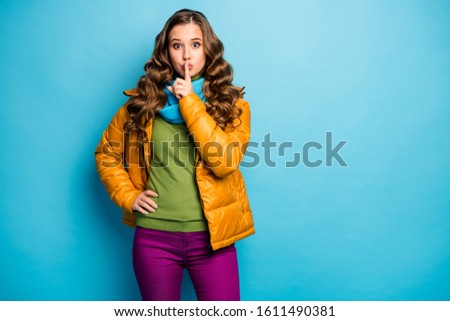 Don't speak! Photo of pretty curly lady holding finger on lips asking keep secret in privacy wear casual yellow overcoat scarf violet trousers isolated blue color background