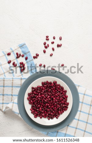 Red beans in a plate on a checkered towel on a white textured background. The view from the top. Space for text.