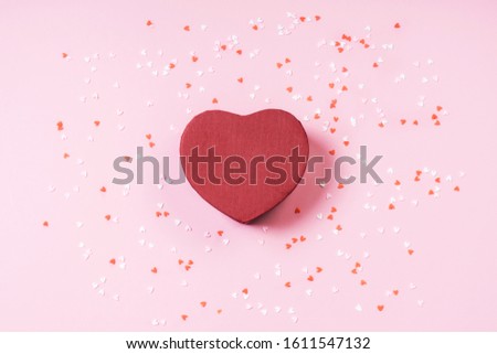 Present box heart on pastel pink background with multicolored confetti Flat lay style