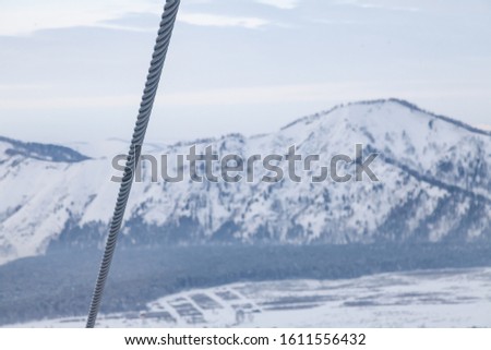 A metal cable from a ski lift at a height with a background of snowy Altai mountains. Rock climbing and construction.