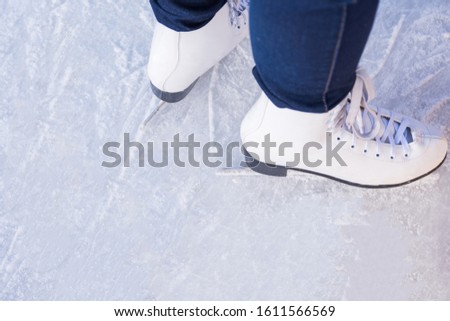 A young woman in white figure skates and blue jeans is standing on the ice, ready for the ride on the rink. Training. Winter entertainment and pastime. Leisure and lifestyle. View from above. Closeup.