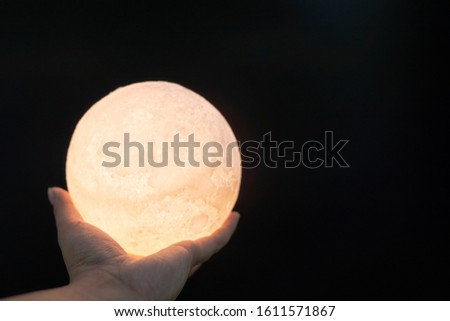 A picture of a hand holding a model of the moon at night