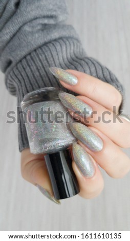 Female hand with long nails gray metallic manicure and a bottle of nail polish