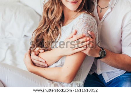 Happy guy and girl in white clothes gently hug each other. Hands - close-up. Holiday Concept - Valentine's Day, International Women's Day