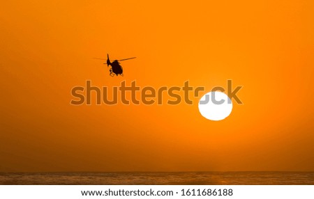 Sihouette of helicopter headed toward setting sun over water. Graphic image with negative space