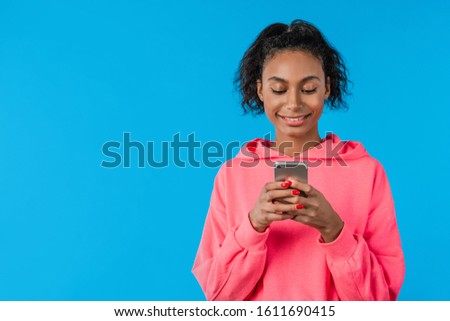 Young afro american woman using mobile phone while standing isolated over blue background