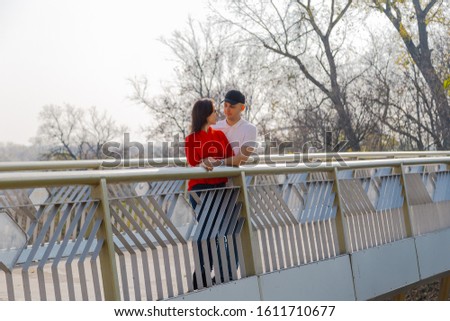 Happy young lovers stand on the iron bridge in autumn weather.