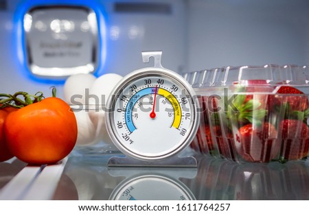 Refrigerator thermometer with colorful food in cold storage unit. Refrigeration safety gauge displaying safe food temperature.