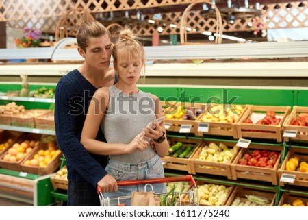 Young couple at the supermarket doing daily shopping walking with cart hugging looking at shopping list concerned just walk out shopping technology Royalty-Free Stock Photo #1611775240