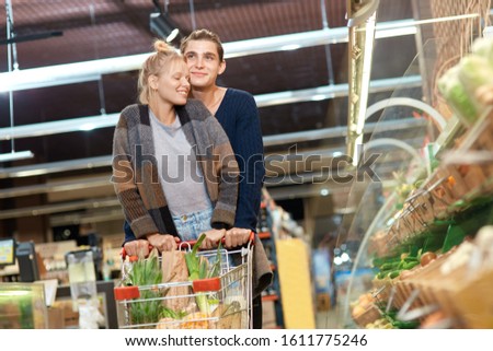 Young couple at the supermarket doing daily shopping walking with cart hugging romantic smiling cheerful just walk out shopping technology Royalty-Free Stock Photo #1611775246