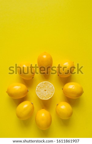 Top view whole and sliced ripe lemons laid out in the shape of a dial on a yellow surface, concept of health and vitamins