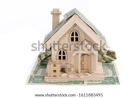 a wooden model of an elegant house covered with dollar bills illustrating real estate investment isolated on white