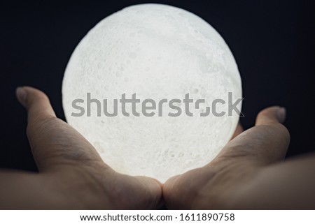 A picture of a hand holding a model of the moon at night